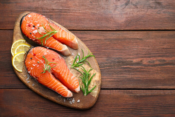Fresh raw salmon steaks with spices, lemon and rosemary on wooden table, top view. Space for text