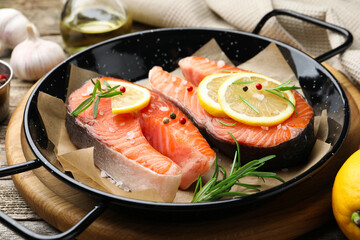 Fresh raw salmon steaks with spices in pan on wooden table, closeup