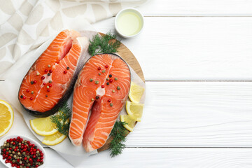Fresh raw salmon steaks with spices, lemon and dill on white wooden table, flat lay. Space for text