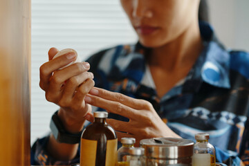Closeup of young Asian woman holding jar of pills in her hands, checking expiration date
