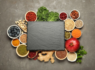 Superfood. Different healthy food products and blank board on grey table, flat lay. Space for text