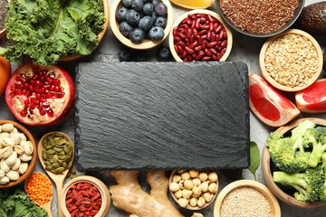 Different superfood products and blank slate board on grey table, flat lay. Space for text