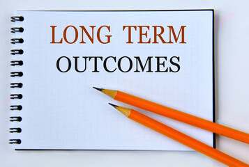 LONG TERM OUTCOMES - words in notebook on white background with pencils
