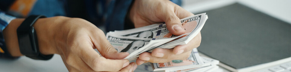 Closeup of hands of unrecognizable female accountant holding bundle of money, while working in office, website header