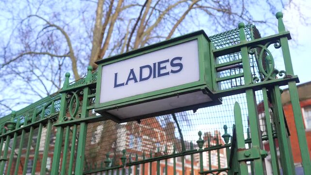 A vintage "ladies" sign on an old outdoor public toilet under sunny skies, nostalgic design and outdated restrooms