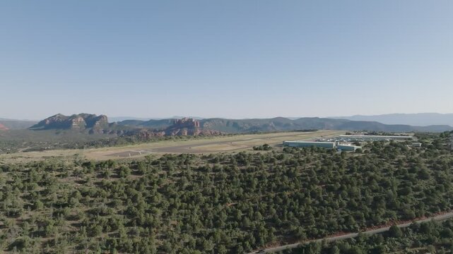 Sedona's Airport and green landscape with distant red rock formations under clear blue skies , aerial view