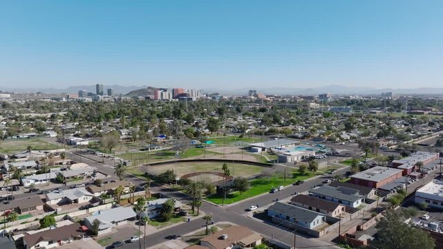 Single family homes in suburb district of Tempe. Sport area with baseball field and palm trees in Arizona, USA. Aerial forward wide shot. Downtown skyline in distance.