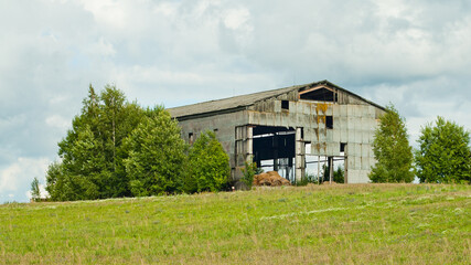 Obraz premium ruined old hayloft, green field in the foreground, grey sky in the background