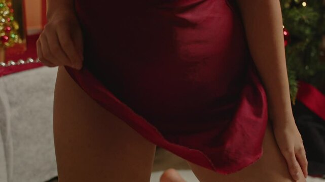A beautiful woman sensual lifts her skirt and reveals her red underwear in front of a decorated Christmas tree