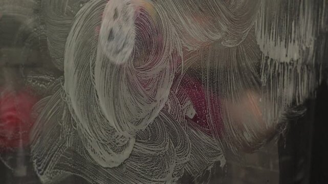 young woman cleaning a glass surface with sponge and soap, removing dirt and limescale, creating swirling patterns