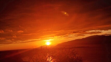 Vibrant sunset over calm waters, silhouetted mountains, and glowing, dramatic red clouds