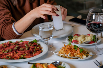 Upper angle shot of the Woman's Hand Holding a Raki Glass at a Seafood Restaurant Table. The table is filled with Turkish mezes, seafood, and a cultural dining experience.