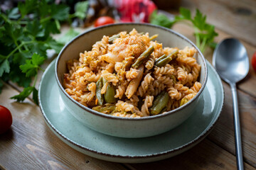 Home cooking: pasta with vegetables and tomato sauce in a light plate on a wooden table. Pasta with vegetables for lunch. Close-up