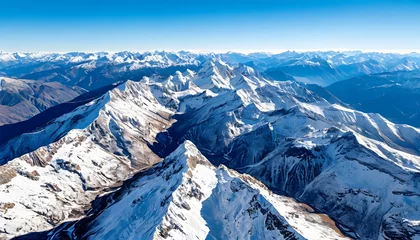 Fototapete An aerial view of huge snow-capped mountain ranges stretching to the horizon under a clear blue sky. © Deamard