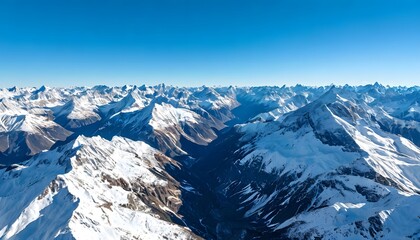 Fototapeta premium An aerial view of huge snow-capped mountain ranges stretching to the horizon under a clear blue sky.