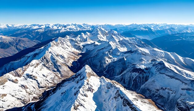 An aerial view of huge snow-capped mountain ranges stretching to the horizon under a clear blue sky.