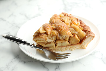 Slice of homemade apple pie and fork on white marble table