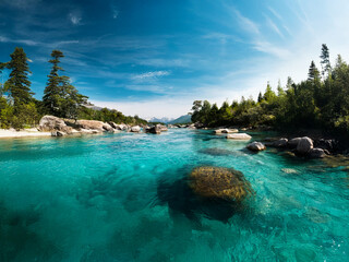 Serene river flows through a pristine landscape. Crystal-clear turquoise water, smooth rocks, and lush greenery create a breathtaking vista under a vibrant blue sky.  The scene evokes tranquility and 