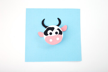 cow craft made from a bottle cap and colored paper with large round eyes on a blue background. Top view photography of a handmade DIY project for kids. Creative and educational recycling craft