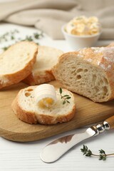 Cut baguette with butter and herbs on white wooden table, closeup