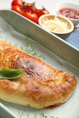 Delicious calzone pizza in baking dish and ingredients on table, closeup