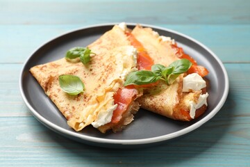 Delicious crepes with salmon, cream cheese and basil on light blue wooden table, closeup