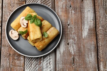 Delicious rolled crepes with mushrooms and basil on wooden table, top view. Space for text