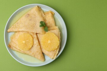 Delicious Crepes Suzette on green background, top view. Space for text