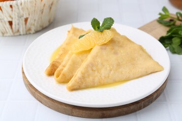 Tasty crepes Suzette on white tiled table, closeup