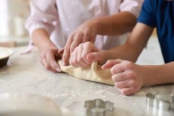 Grandmother and her grandson kneading dough at white marble table in kitchen, closeup