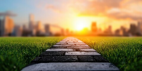 A serene pathway leads through lush grass towards a glowing sunset, framed by a city skyline in the distance.