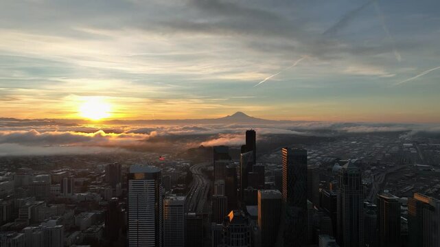 Sunrise casts light on clouds above Seattle with Mount Rainer in the distance