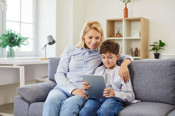 Mother, nanny and child son at home sitting using digital computer tablet applications, choosing goods shopping in internet store, playing games, spending time online, watching movie, smiling surfing
