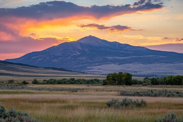 Obraz premium A stunning sunset view behind a mountain range, featuring vibrant hues of orange, pink, and purple in the sky with grassy fields in the foreground