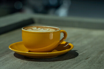 A yellow cup of hazelnut latte placed on a wooden table, photographed at night with an eye level angle