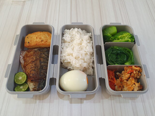 Flat lay. School lunch bento box with vegetable, grilled fish, boiled eggs and sambal