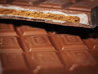 A close-up of a milk chocolate bar, showing a crispy layered filling of golden biscuit and creamy white chocolate against a soft fabric background.