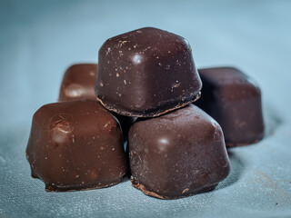 A close-up of a stack of dark chocolate candies with a rich, smooth finish arranged on a soft fabric background. Perfect for gourmet or dessert themes.