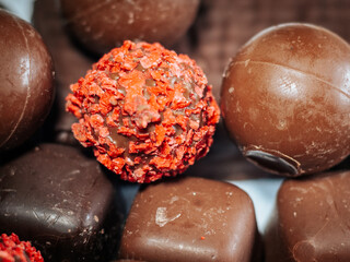 A detailed close-up of chocolate truffles featuring bright red chips surrounded by smooth chocolate balls and square shapes. Perfect for holiday or dessert themes.