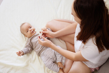 A mother is joyfully playing with her baby on a soft blanket at home. The room is filled with...