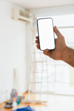 Vertical image, unrecognizable hand holding a phone with tools in the room blurred in the background