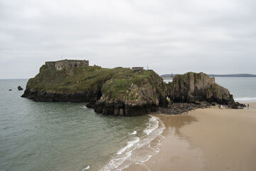 Castle Beach - Serene coastal landscape with a rocky island featuring a historic fort, calm...