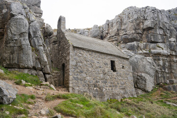 This image features St Govan's Chapel, a stone building nestled against rugged cliffs, with a steep slate roof and narrow windows, blending beautifully with its serene, natural surroundings.