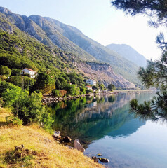 Fototapeta premium Scenic lakeside view with mountains, serene mood, reflection of trees and buildings, natural landscape