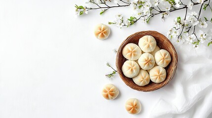   A wooden bowl holding dumplings beside a blooming twig on white