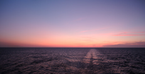 Obraz premium sunrise sun is setting over the ocean as beautiful backdrop for web page banner template. sky is beautiful mix of pink and purple. water is calm and still, with a cruise ship's wake off stern.