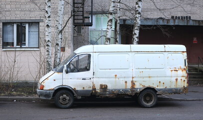 An old white rusty minibus stands near the walls of the apartment building, Belysheva Street, St....