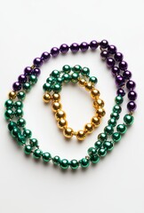 Obraz premium Colorful beads in vibrant hues of green, purple, and gold arranged in an artistic pattern on a clean white background for festive celebrations and decorations