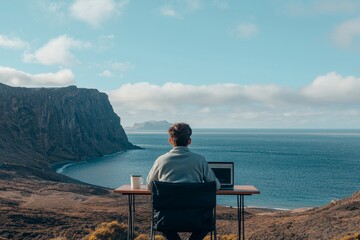 Fototapeta premium A man of Caucasian descent is seated on a wooden chair, focusing on his work remotely using a laptop, with mountains and the sea visible in the background, illustrating the concept of a Digital Nomad
