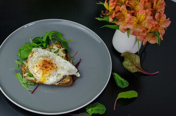 Fried egg on a bread roll with greens on a grey plate